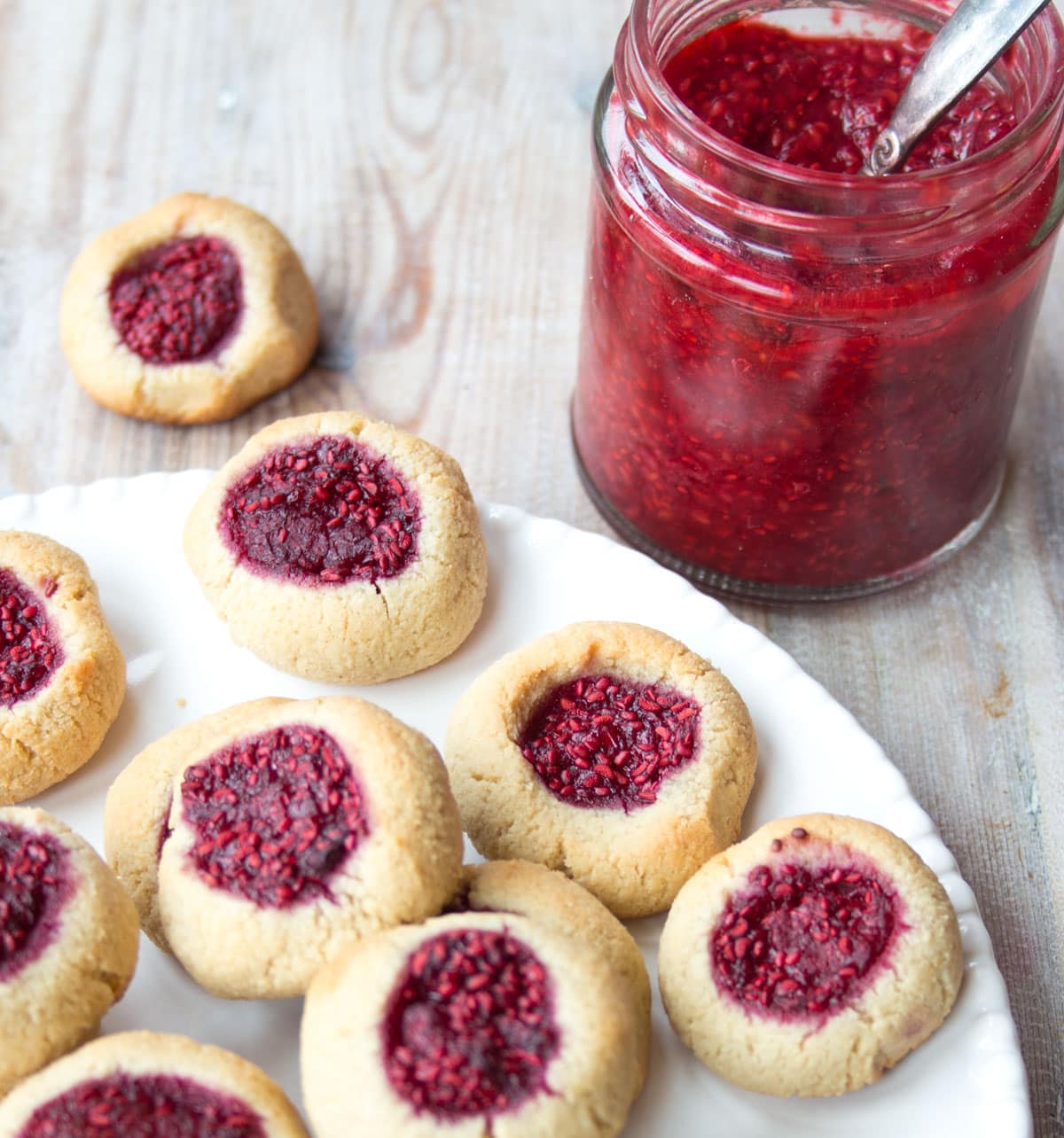 Thumbprint cookies wth a raspberry jam filling and a jar of jam.