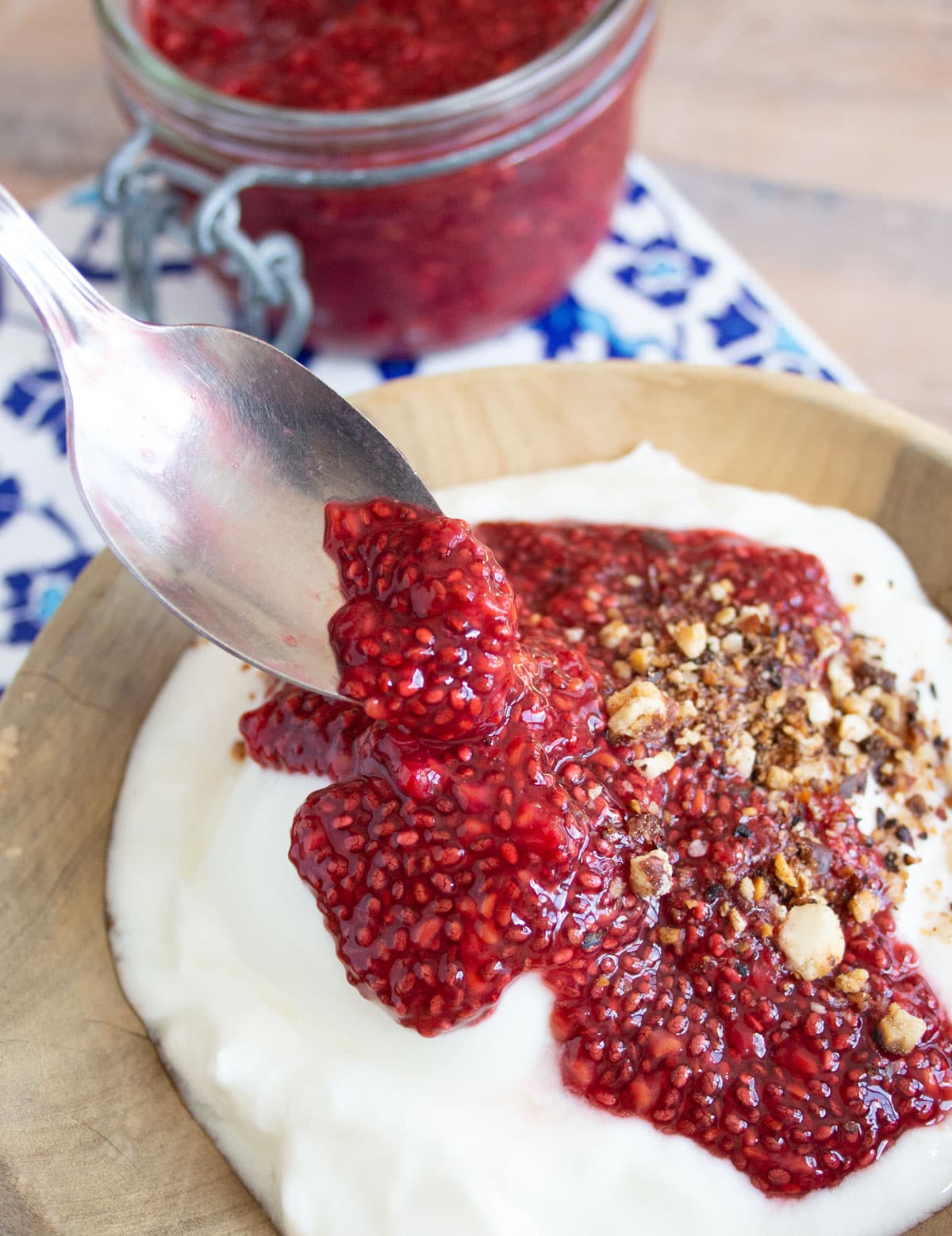 Spooning raspberry jam onto a bowl with yogurt.