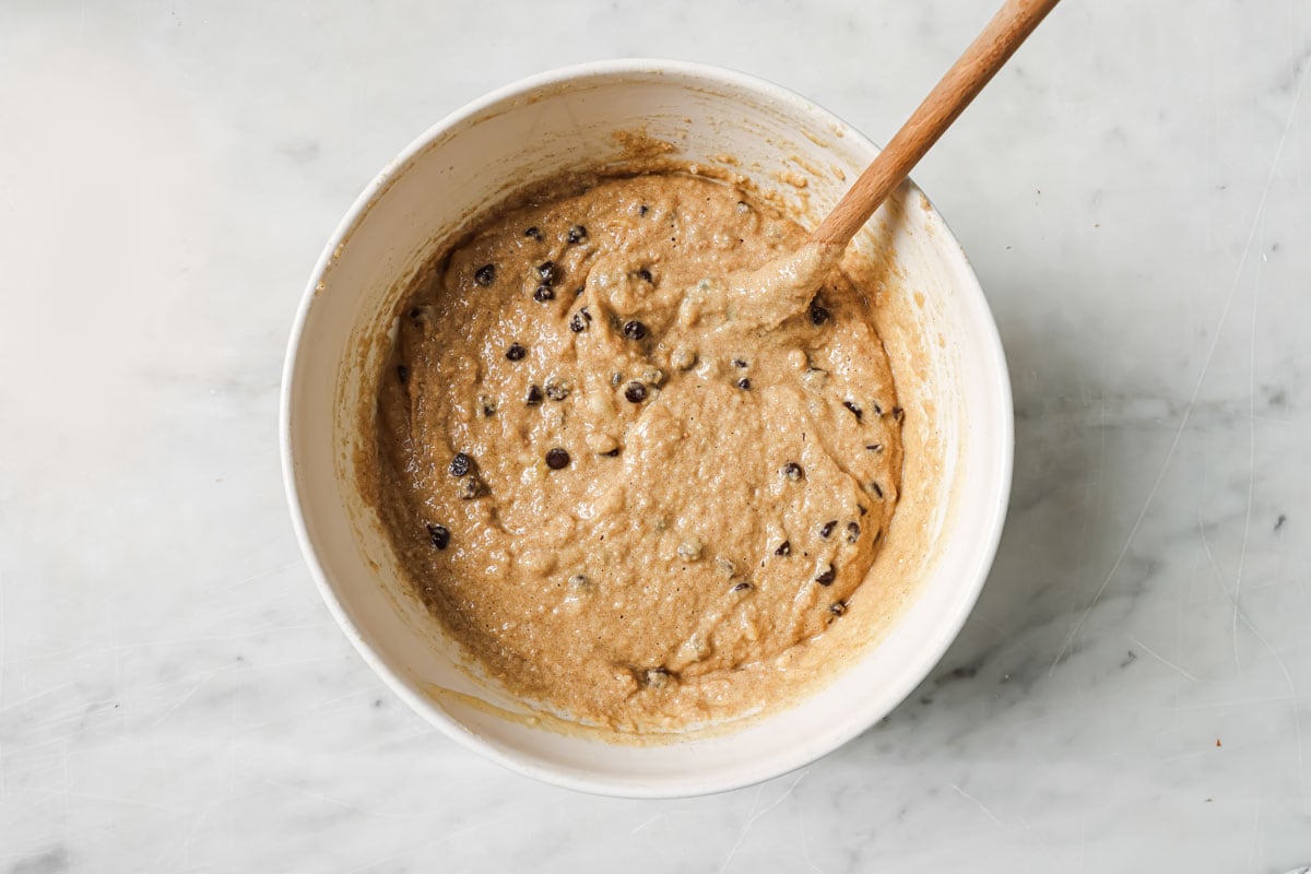 Banana bread batter with chocolate chips in a bowl and a spatula.