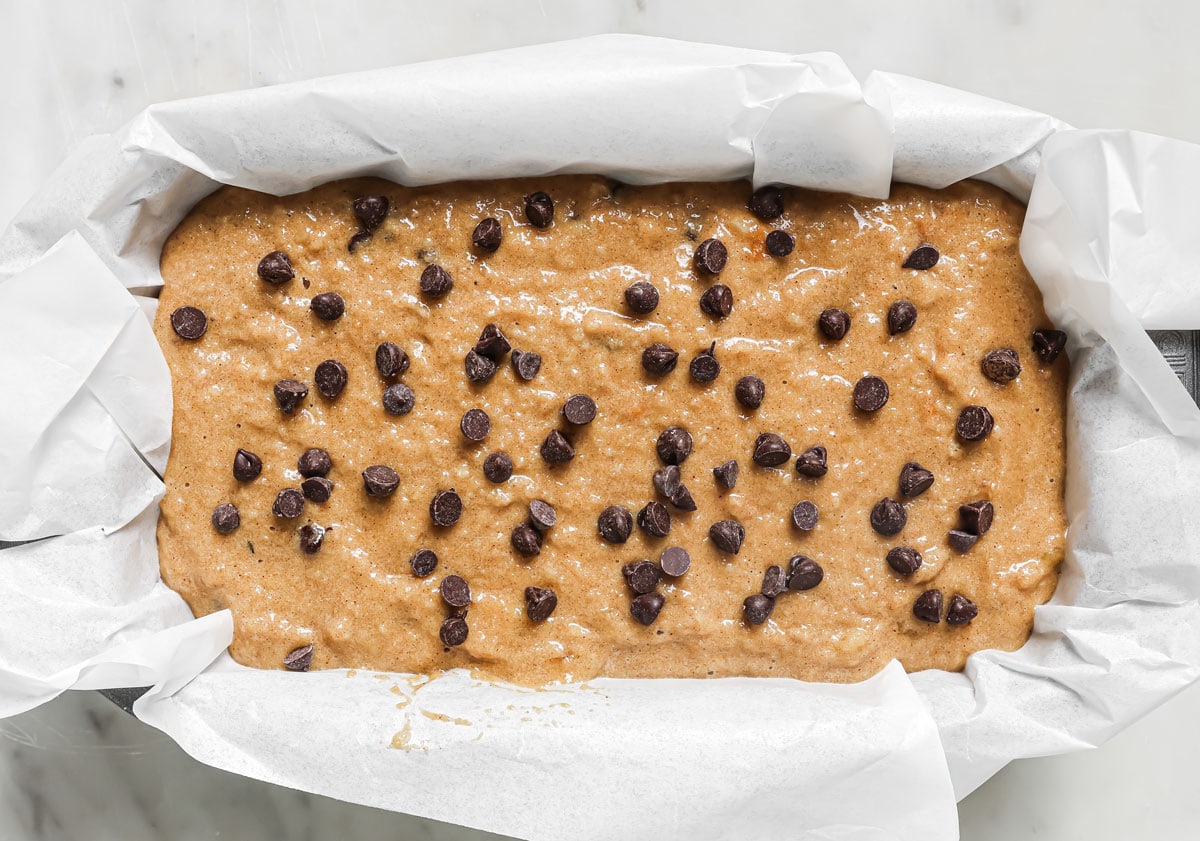 Banana bread batter topped with chocolate chips in a pan lined with parchment paper.
