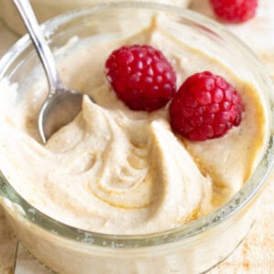 A glass bowl with peanut butter protein fluff and 2 raspberries.