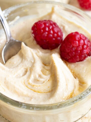 A glass bowl with peanut butter protein fluff and 2 raspberries.