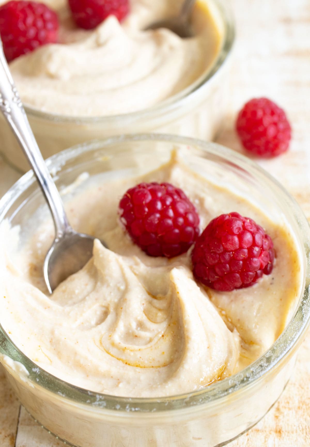 Peanut butter protein fluff in a glass bowl with raspberries and a spoon.