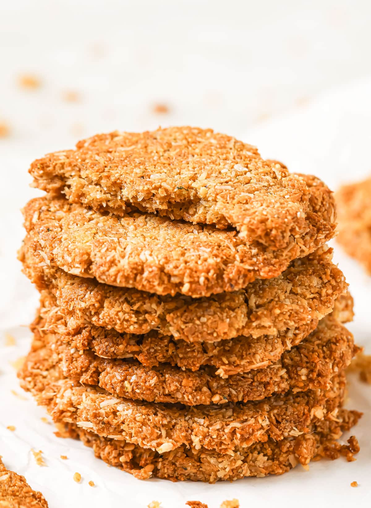A stack of keto anzac biscuits, the top biscuit is broken in half.