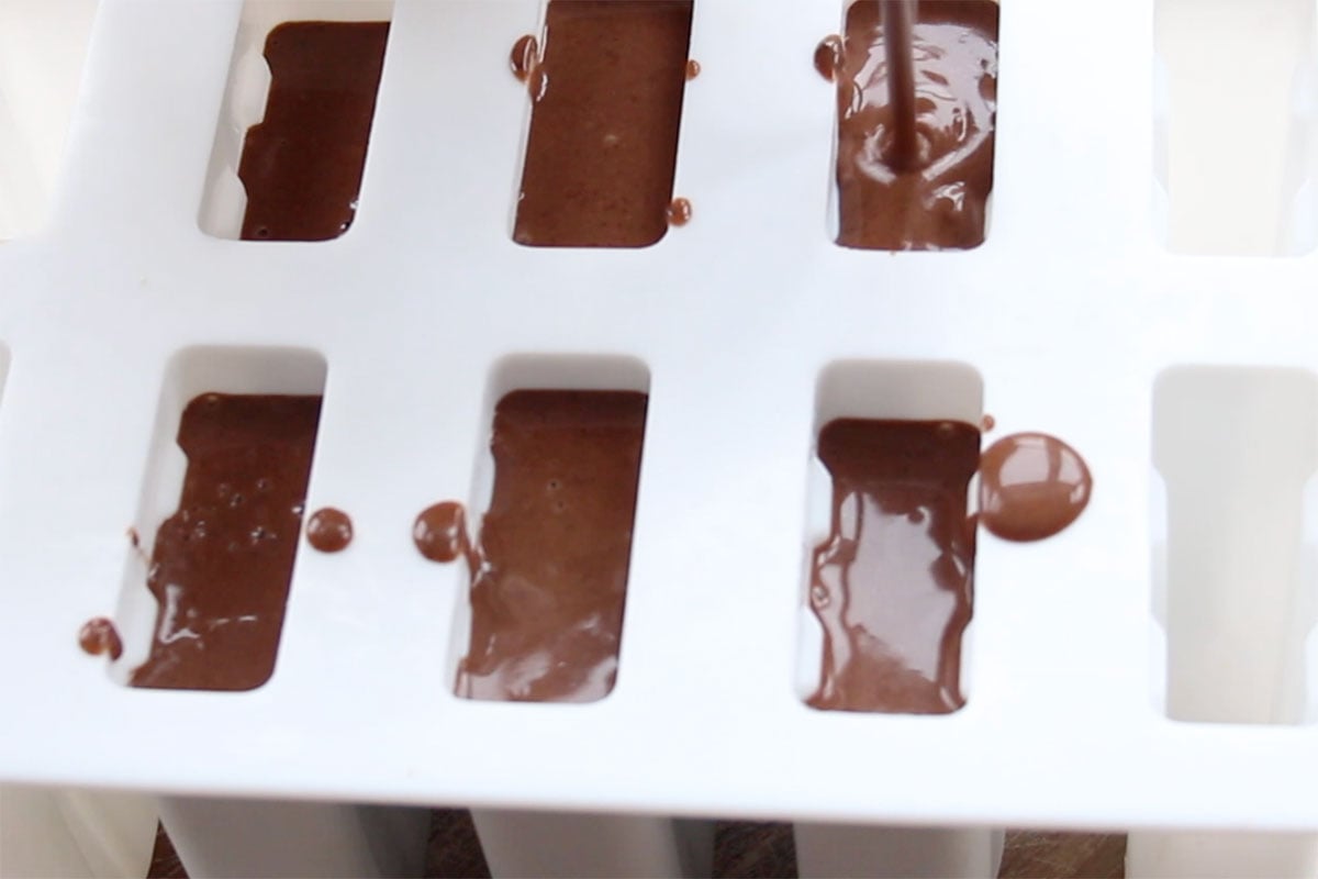 Pouring the chocolate mixture into a white silicone popsicle mold.