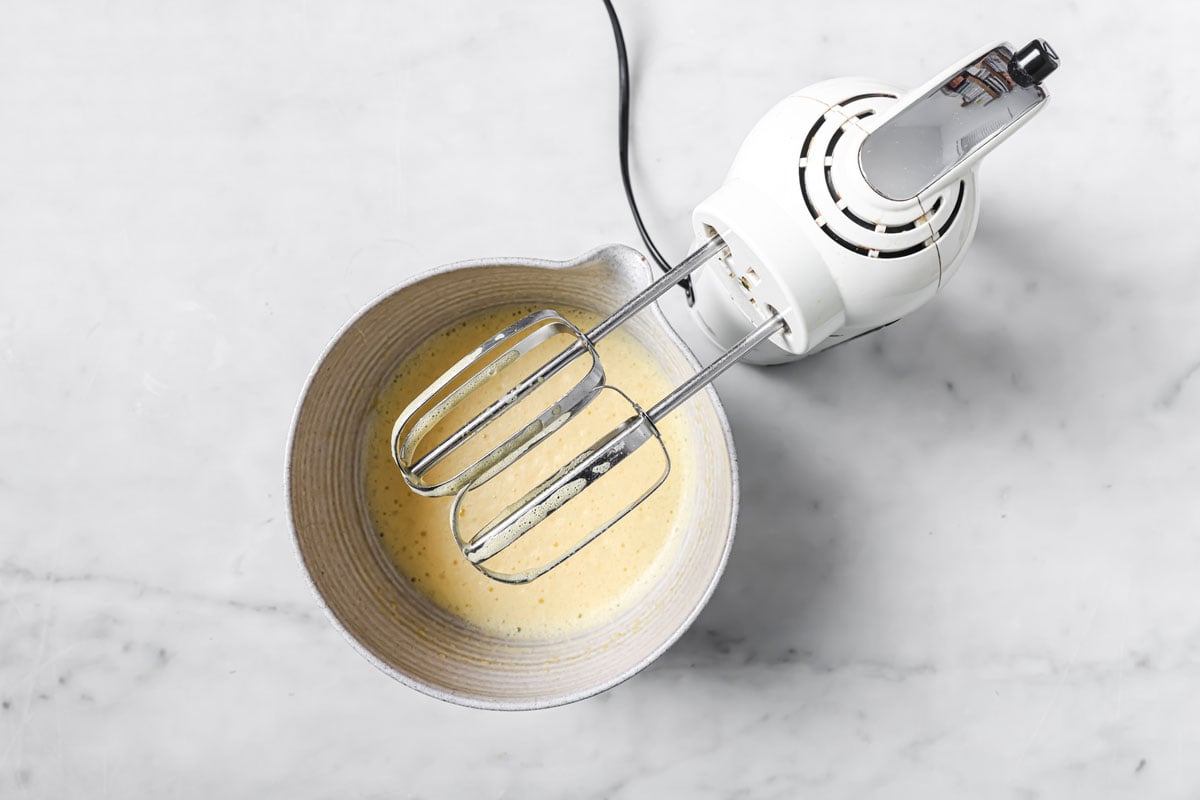 Whisked eggs in a mixing bowl and an electric blender.