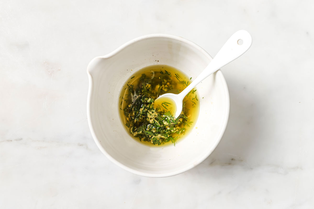 Olive oil herb dressing in a bowl with a spoon.