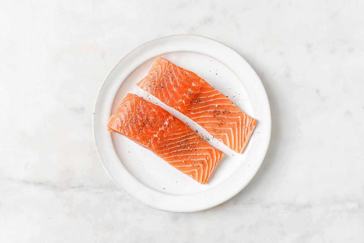 Two salted and peppered raw salmon fillets on a plate.