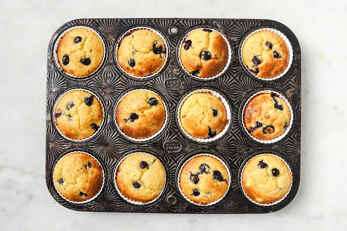 12 baked blueberry muffins in a muffin pan.