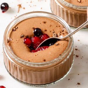 Chocolate protein pudding in a glass bowl decorated with cocoa powder and mixed berries and a spoon.