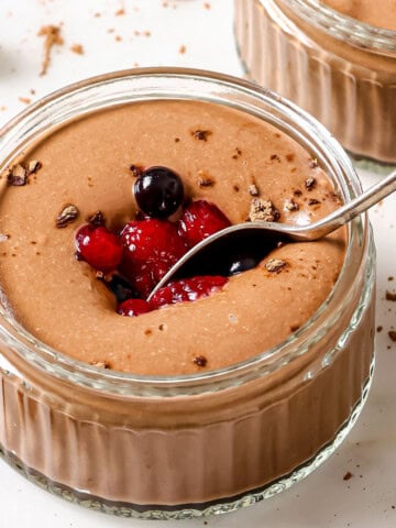 Chocolate protein pudding in a glass bowl decorated with cocoa powder and mixed berries and a spoon.