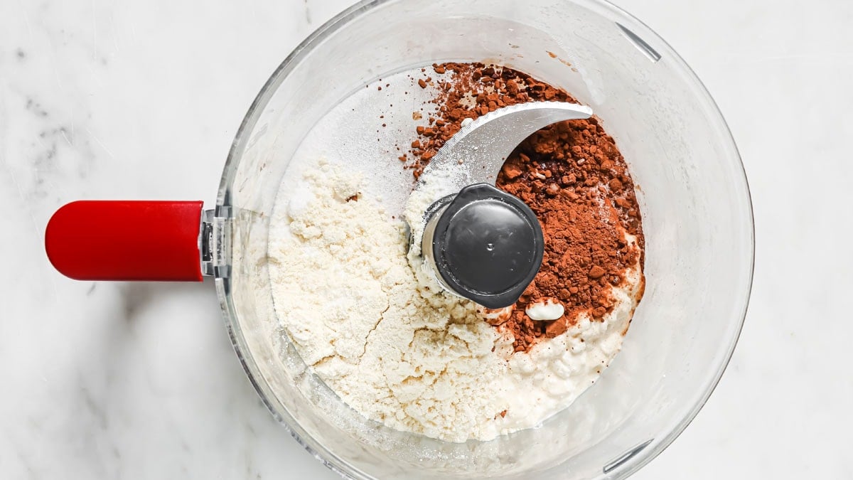 Protein powder, cocoa powder, sweetener, cottage cheese and vanilla in a food processor bowl.