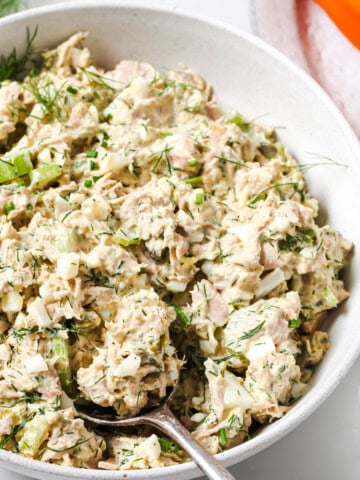 A bowl with tuna egg salad and a spoon.