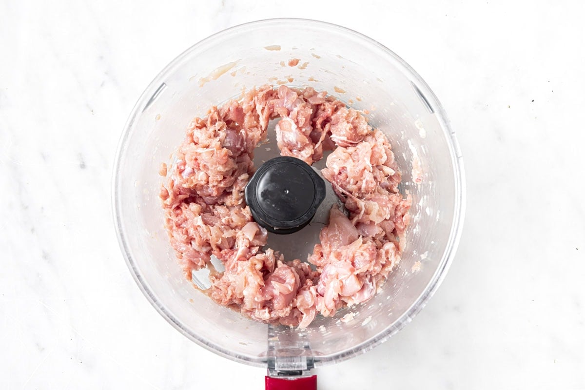 Blended chicken thighs in a food processor bowl.