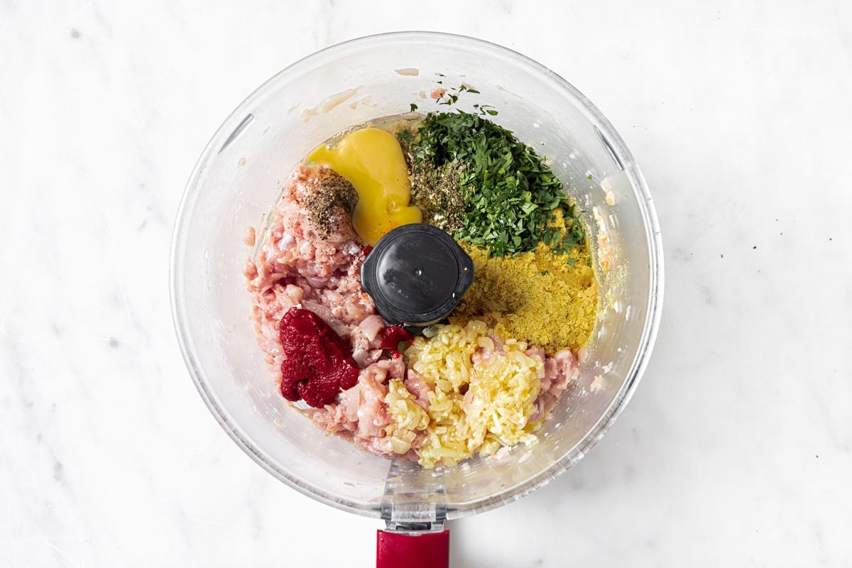 Ingredients to make chicken meatballs in a food processor bowl.