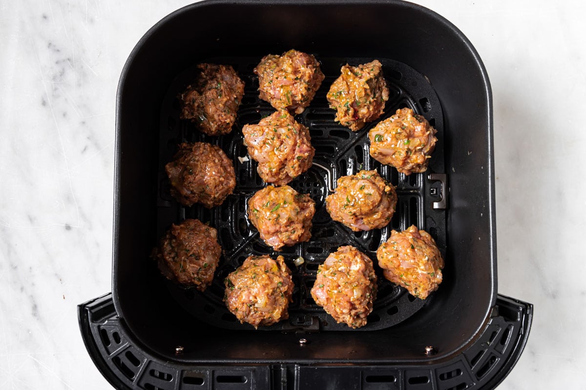 Raw meatballs spaced out in the airfryer basket.