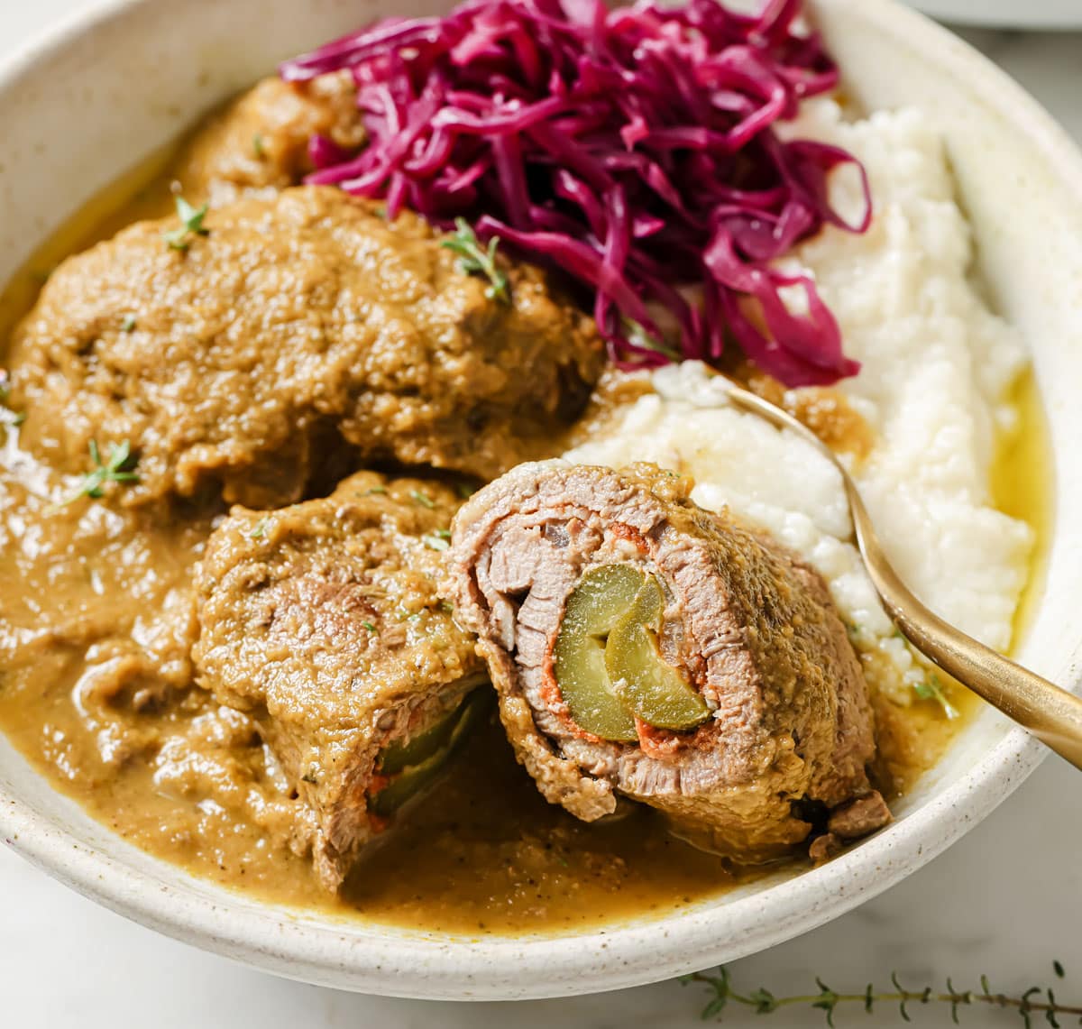 A beef roulade sliced in half showing the inside on a plate.