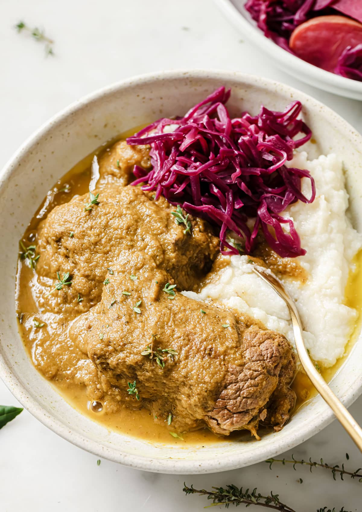 Rouladen in a thick gravy with red cabbage and mash on a plate.