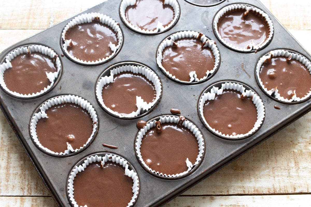 Muffin batter in paper cups in a muffin pan.