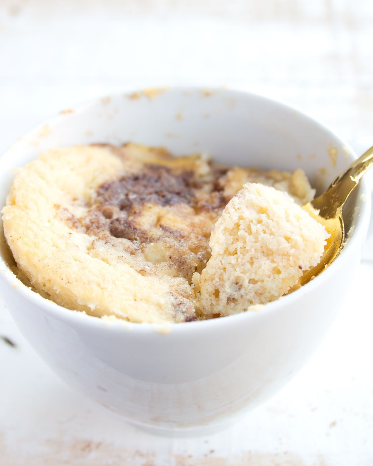 Coconut flour mug cake with a cinnamon swirl and a golden spoon.