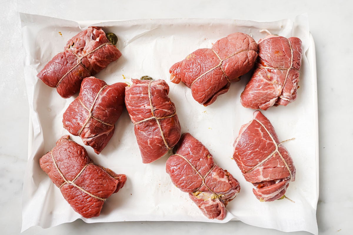 Filled beef rolls secured with string on a tray.