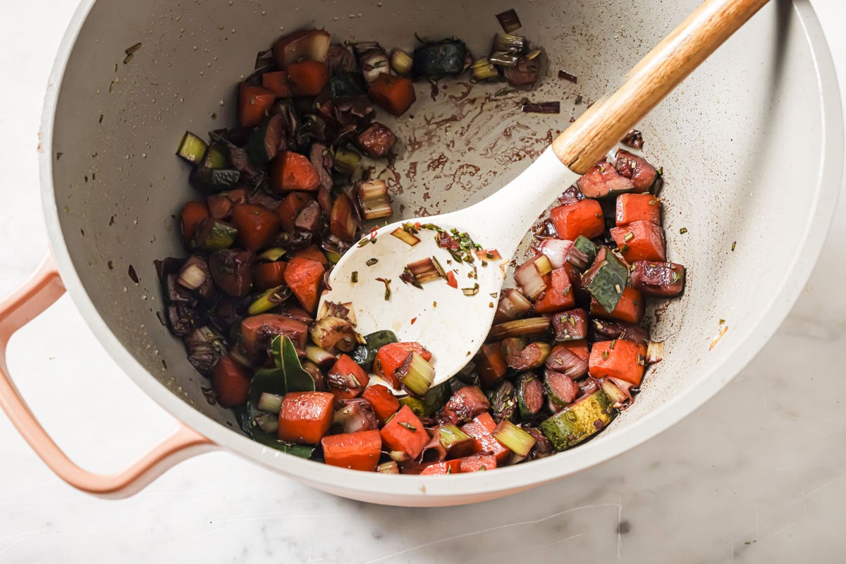 Chopped vegetables with red wine in a pot and a spoon.