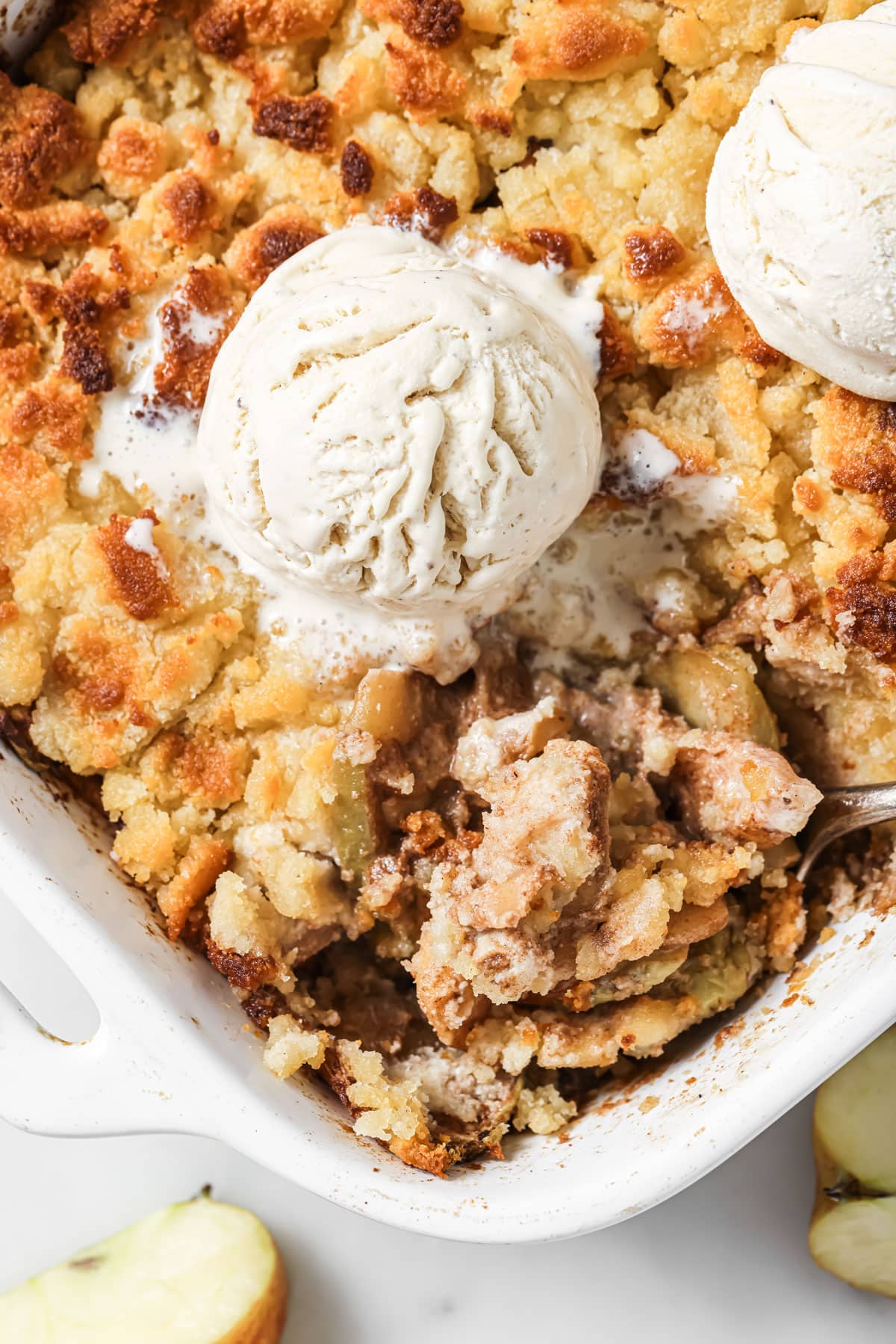 A pan with aple crumble topped with ice cream scoops.