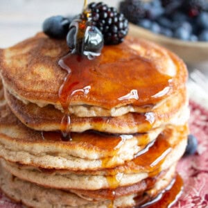 A stack of fluffy cinnamon pancakes topped with sugar free syrup and berries.