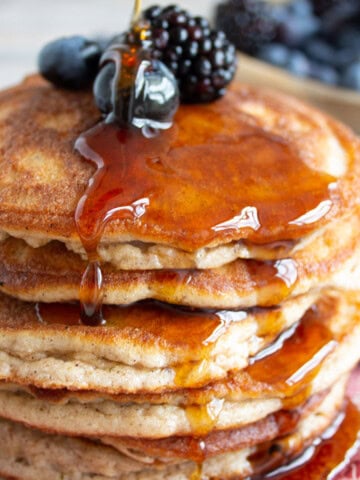 A stack of fluffy cinnamon pancakes topped with sugar free syrup and berries.