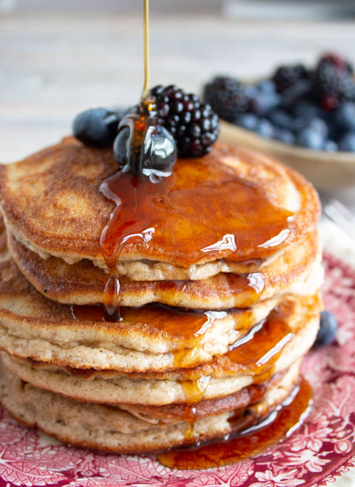 A stack of fluffy cinnamon pancakes made with coconut flour topped with berries and a drizzle of sugar free syrup.