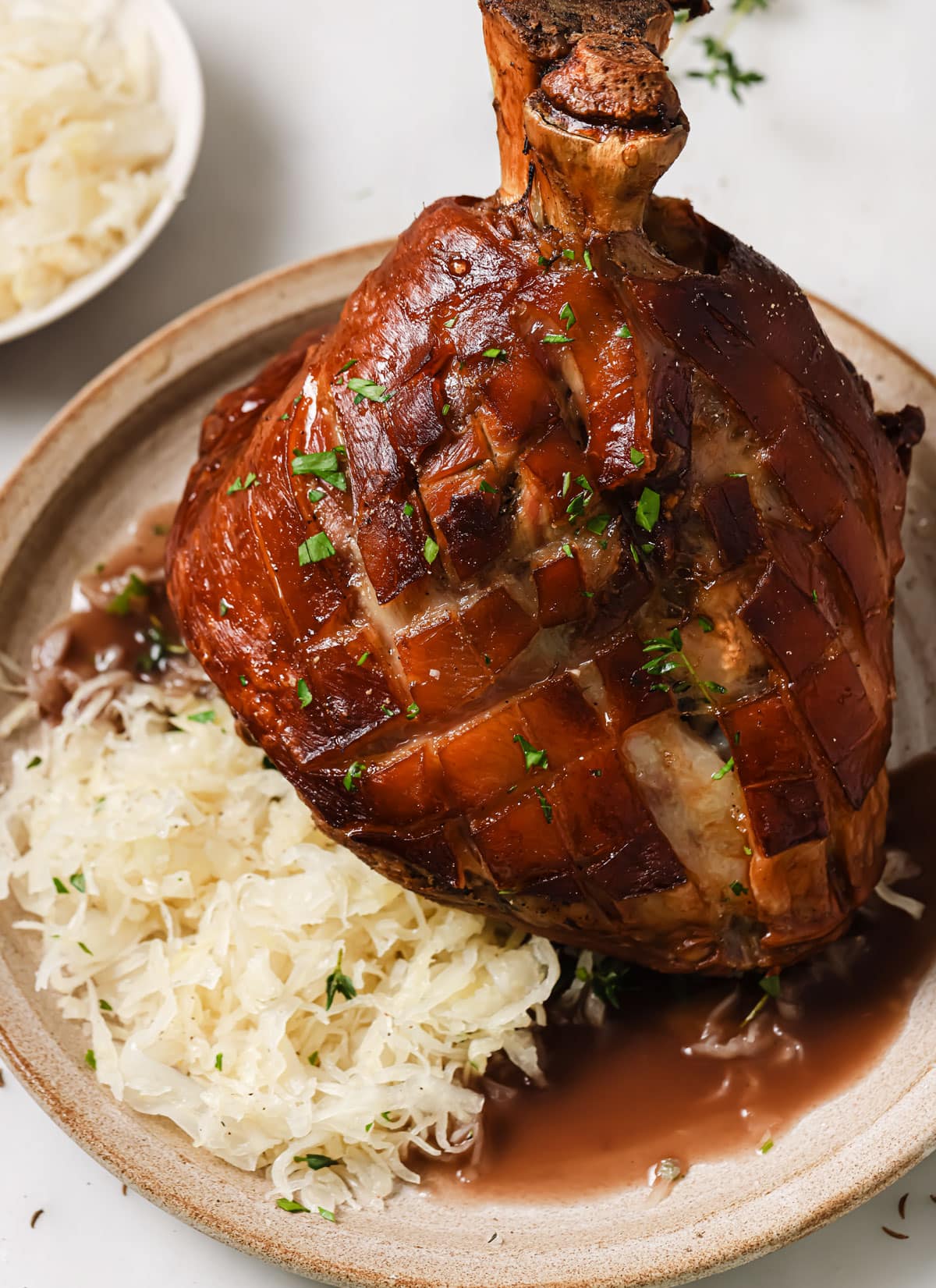 A roasted pork knuckle with scored crispy skin on a plate with sauerkraut and gravy.