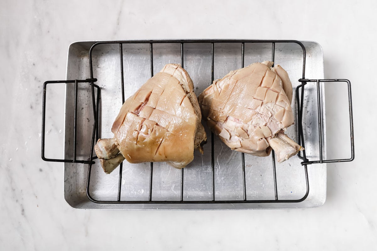 Two boiled pork knuckles, skin scored, on a roasting trivet.