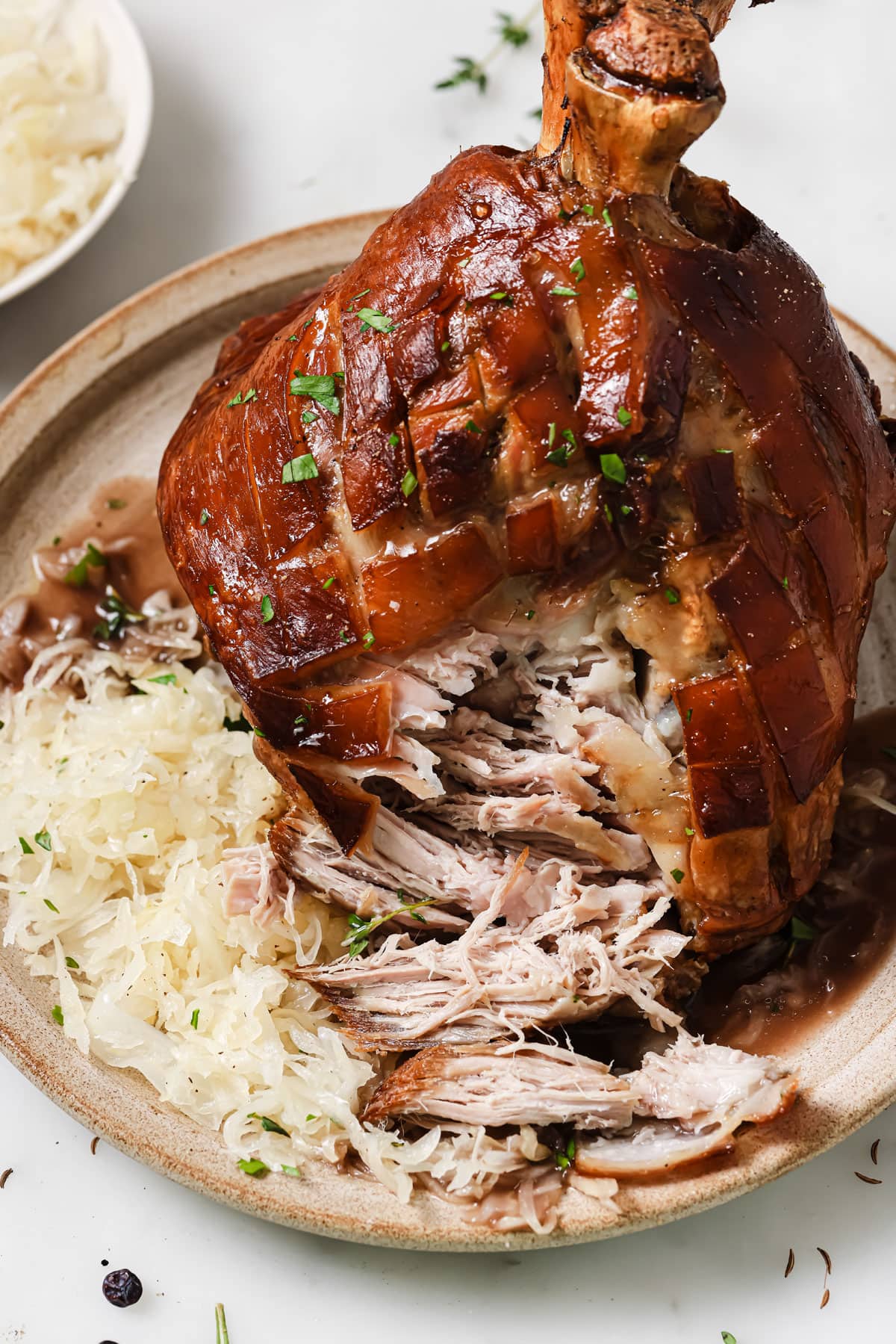 A roasted pork knuckle served on a plate with gravy and sauerkraut. The knuckle is cut open and some of the meat has been pulled out.