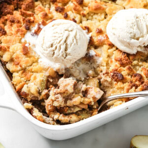 A sugar free apple crumble topped with 2 scoops of vanilla ice cream and a spoon.