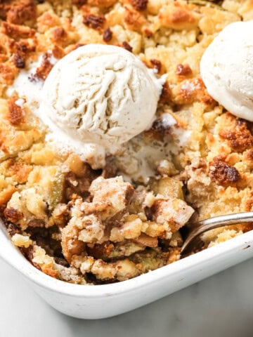 A sugar free apple crumble topped with 2 scoops of vanilla ice cream and a spoon.