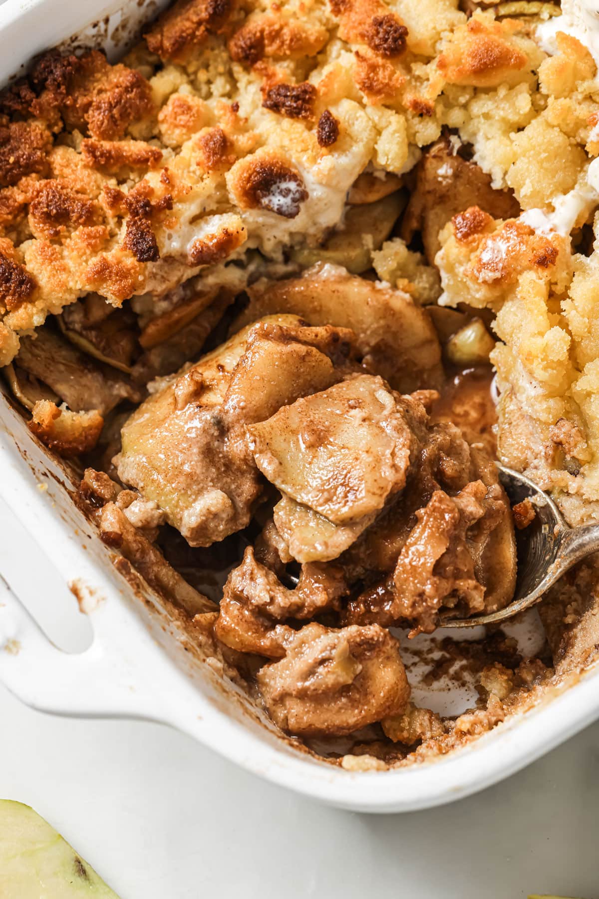 A sugar free apple crumble in a white casserole dish and a spoon.