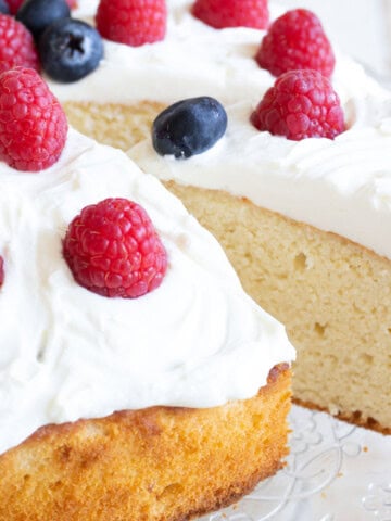 A slice of keto almond flour cake with a mascarpone frosting and berries being removed from the cake.