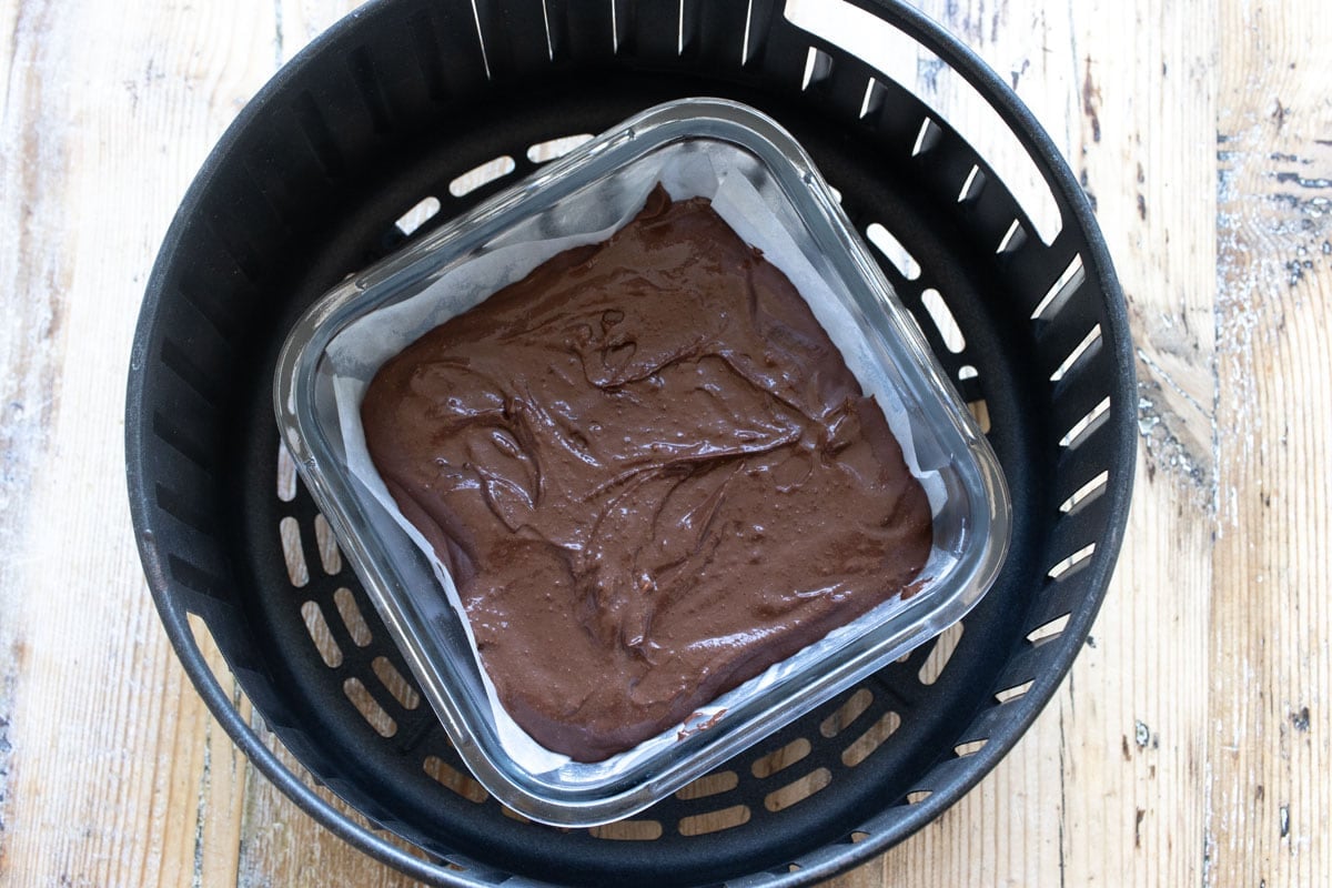 Brownie batter in a parchment paper lined dish in the air fryer basket.