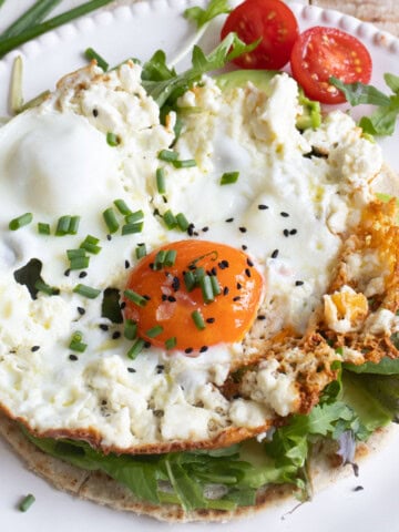 A feta fried egg on a tortilla with lettuce leaves, avocado slices and cherry tomatoes and sprinkled with chopped chives and nigella seeds.