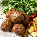 Juicy pork meatballs on a plate served with roasted vegetables and salad leaves.