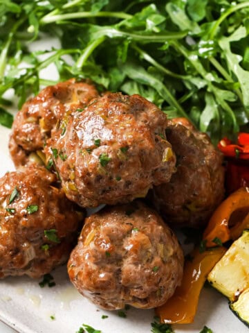 Juicy pork meatballs on a plate served with roasted vegetables and salad leaves.