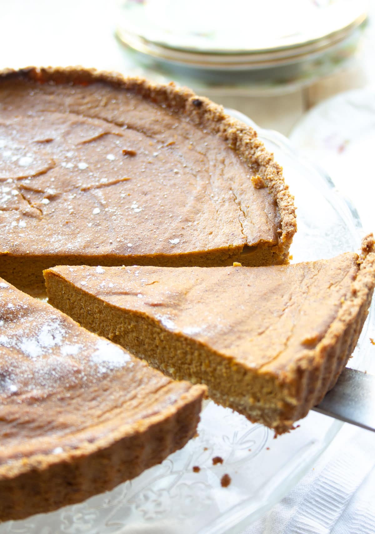 Taking a slice from a sugar free pumpkin pie on a cake stand.