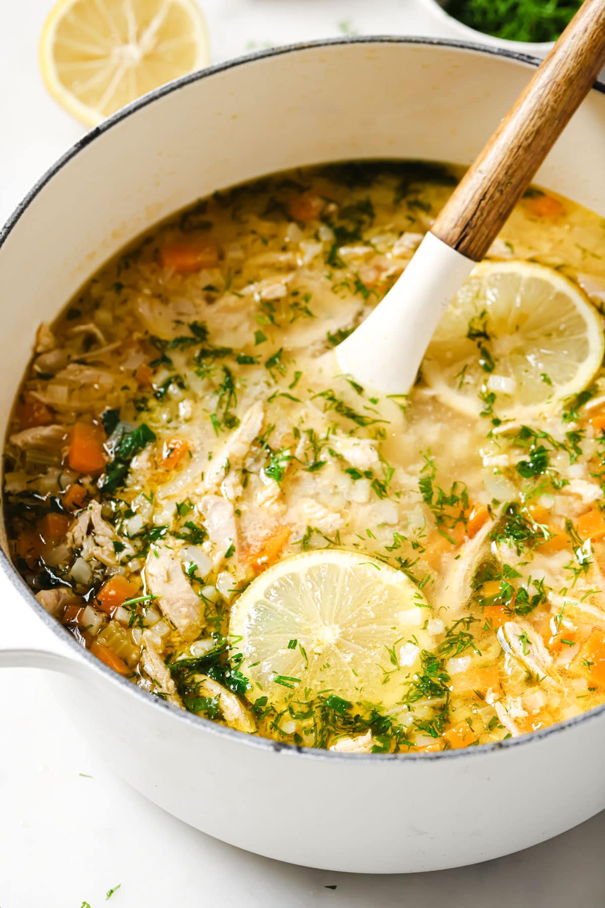 A saucepan with lemon chicken soup and a ladle.