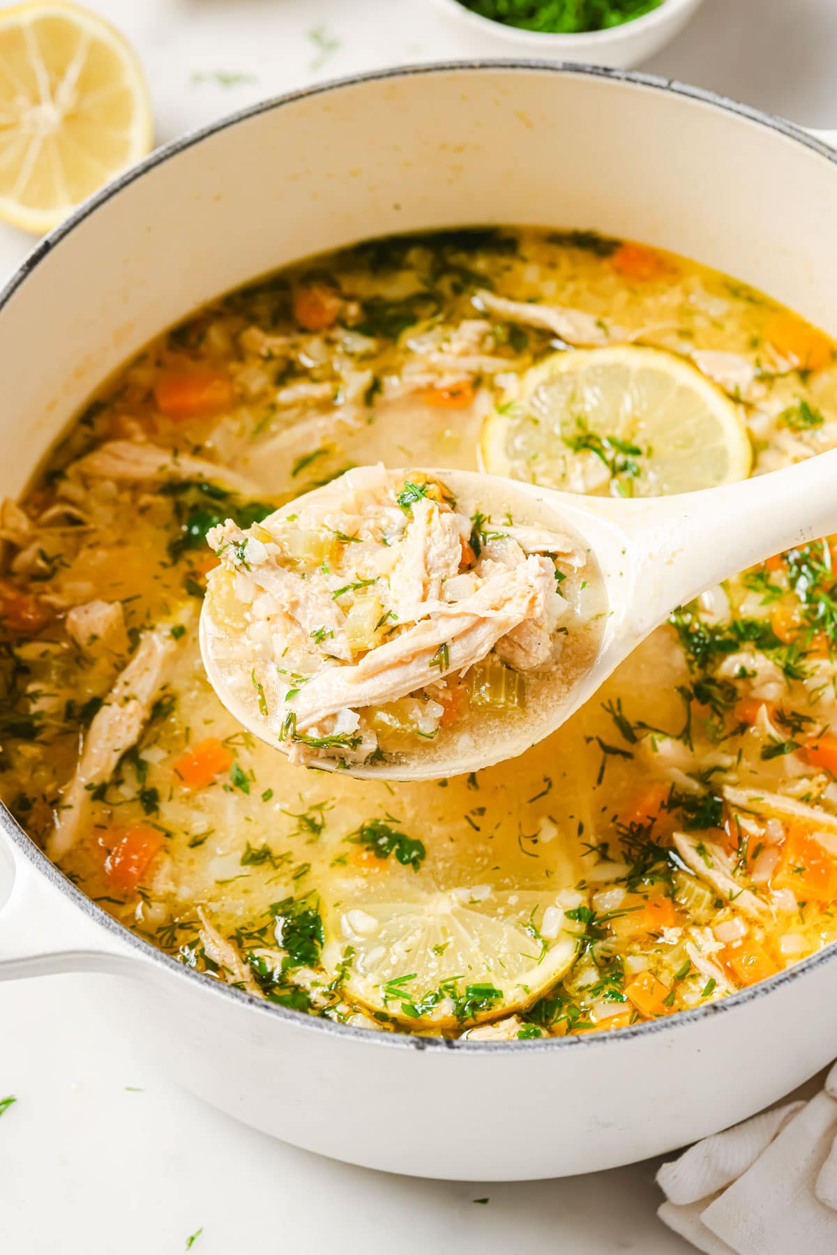 A full ladle with lemon chicken soup and a pot of soup.