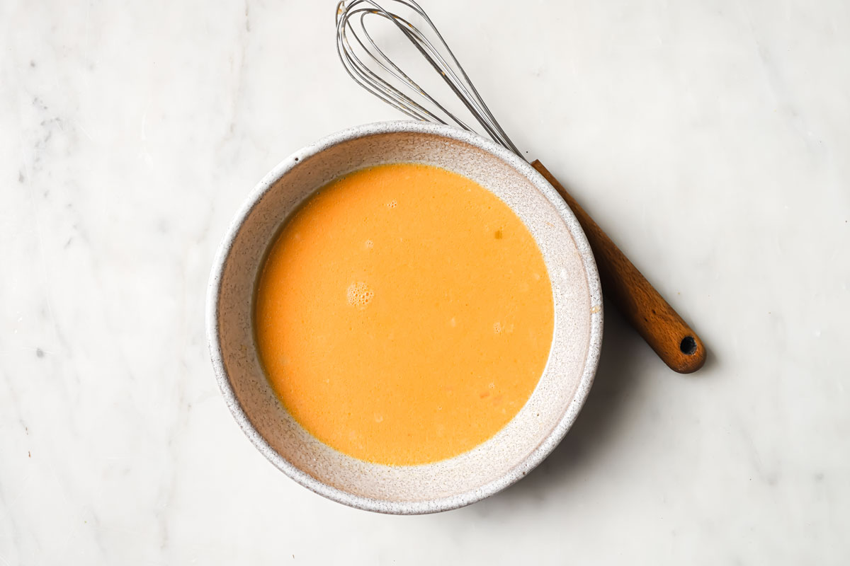 Egg mixture in a bowl and a whisk.