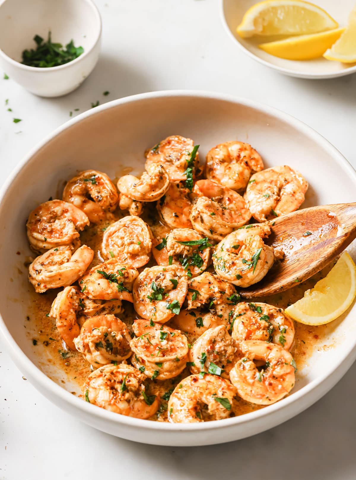 Baked shrimp in a bowl with lemon slices and chopped parsley.