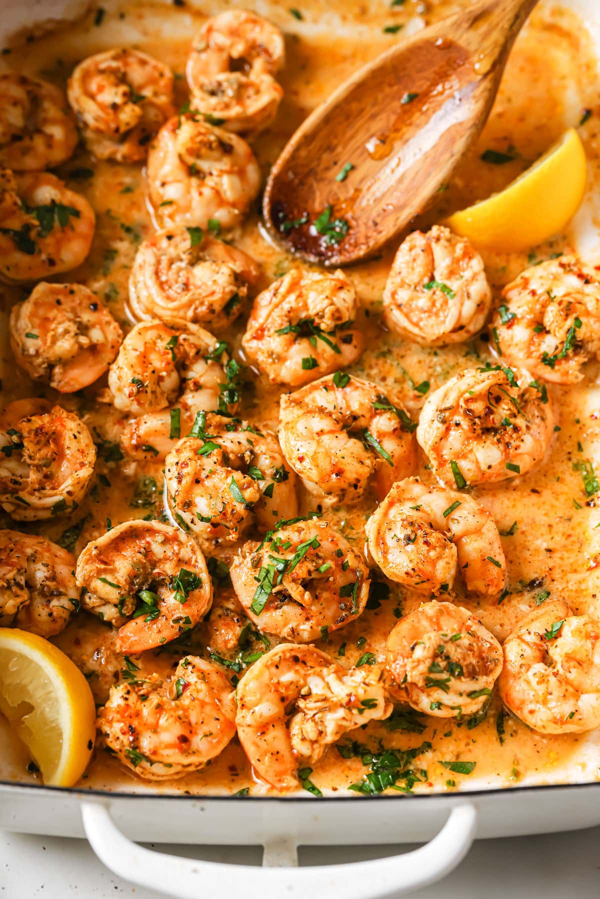 Oven baked shrimp in a baking tray with a wooden spoon and lemon slices.