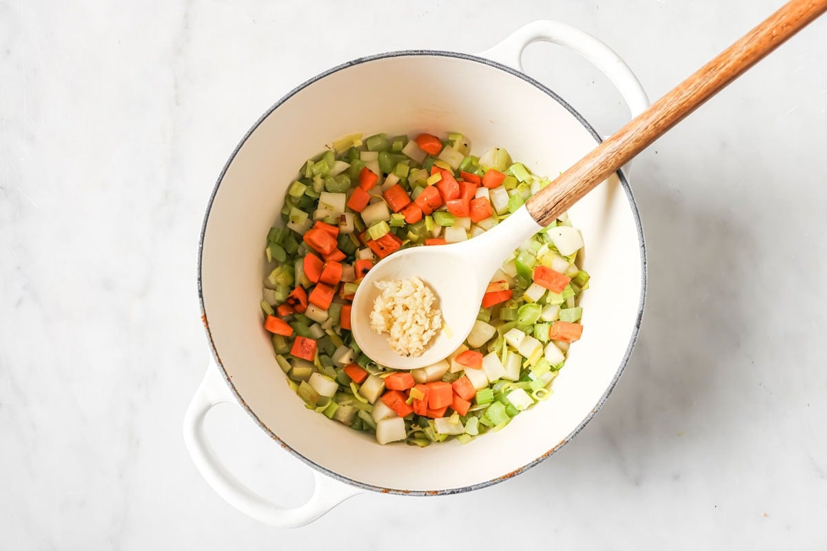 Adding chopped garlic to the soup pot.