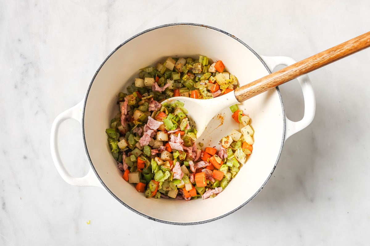 Chopped vegetables and bacon in a pot.