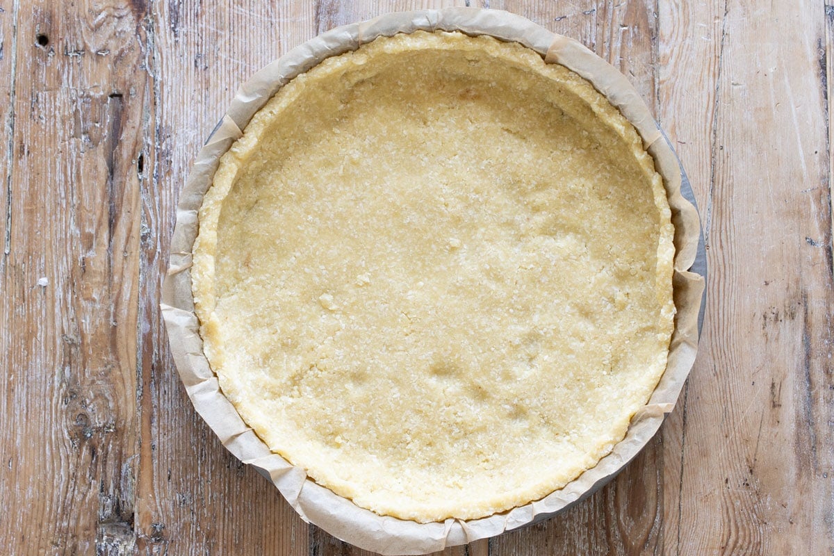 The unbaked tart crust pressed in a pie pan lined with parchment paper.